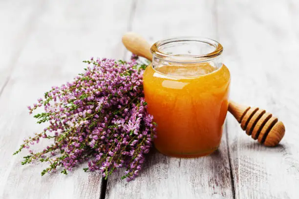 Delicious fresh honey in pot or jar and flowers heather on wooden vintage shabby background.