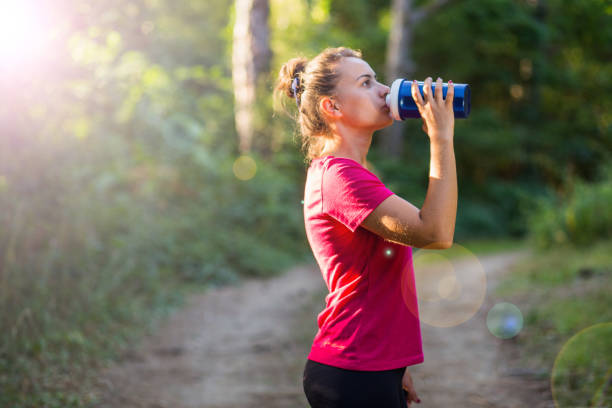 istock White girl drinks water from a shaker after the workout in the woods 838325138