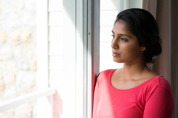 istock Thoughtful young woman looking through window 838330840