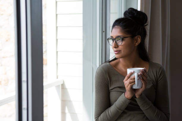 istock Woman with coffee cup by window 838331582