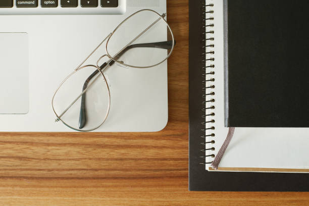 istock Ordinary objects on the table: glasses over the laptop and notebook with paper near by, top view 838338332