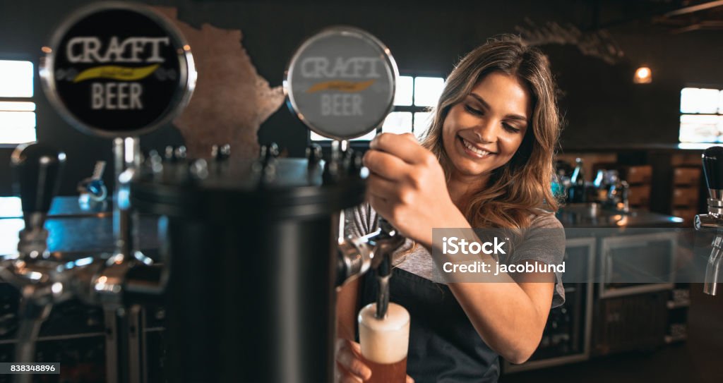 Female bartender tapping craft beer in bar Beautiful young woman pouring beer into the glass. Female bartender tapping craft beer in bar. Bartender Stock Photo