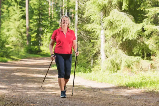 Nordic walking active senior woman working out in the forest and enjoying beautiful summer day.
