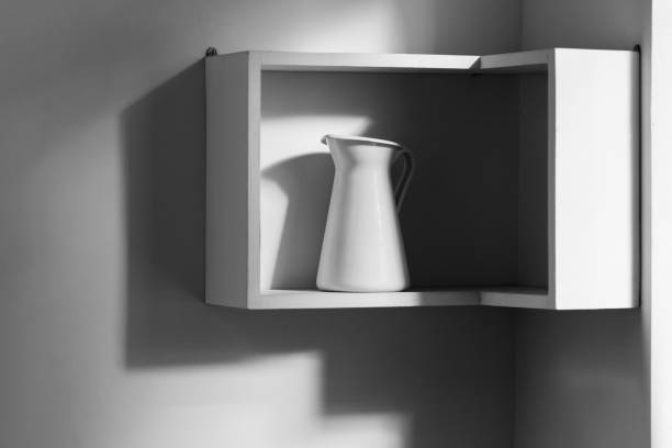 Minimalist interior of white modern kitchen. One isolated jug on shelf and light from window