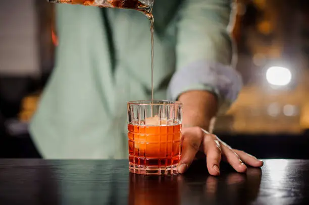 bartender pouring the red cocktail into the glass with iceball