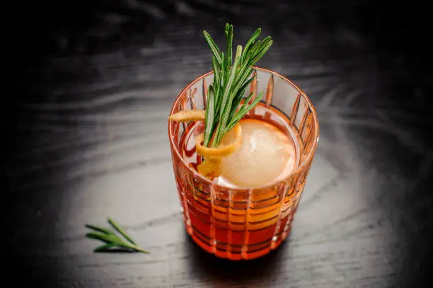 Red alcohol cocktail with rosemary, orange peel and iceball close up