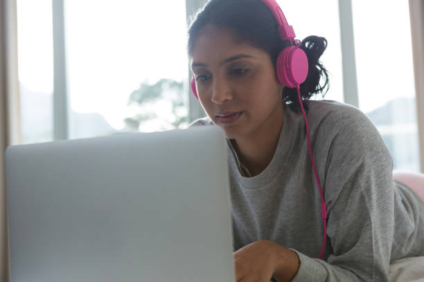 istock Woman listening to music while using laptop on bed 838395892