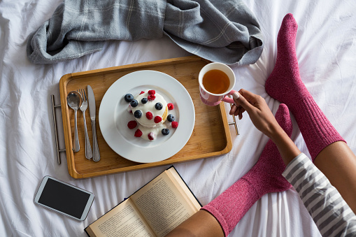 Low section of woman with book having breakfast on bed at home