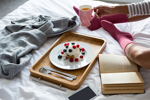 Low section of woman wih book doing breakfast on bed at home