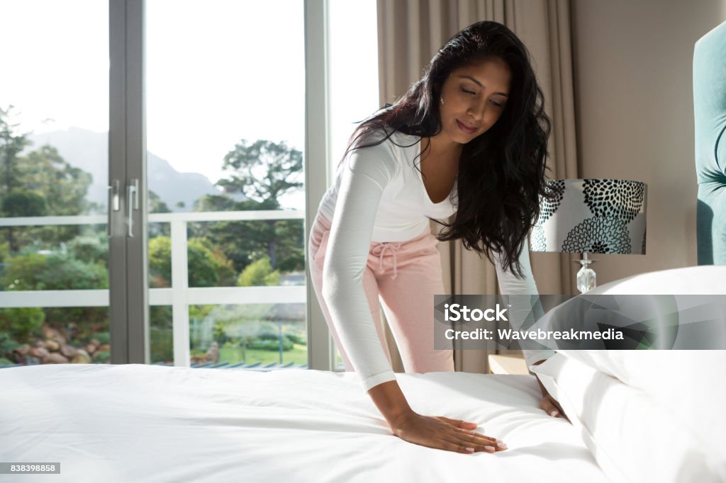 Young woman making bed at home Young woman with long hair preparing bed at home Bed - Furniture Stock Photo