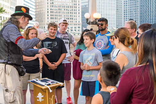 Chicago, IL, August 17, 2017: Downtown Chicago, a street performer magician entertains tourist families. Chicago attracts millions of visitors each year.
