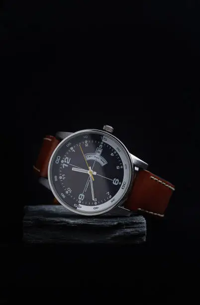 Photo of Wrist watch with a black dial on a gray stone with a dark background.