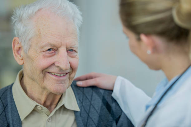 Comforting Doctor A Caucasian female doctor is wearing medical clothing. She is with an elderly man wearing casual clothing. They are indoors in a medical center. The doctor is comforting the man. lymphoma photos stock pictures, royalty-free photos & images