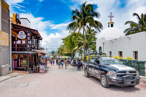 People walking along the 5th Avenue in Playa del Carmen during a summer day. The street is the shopping and restaurant centre in downtown of the city. Police car parked to the right in the picture.