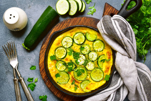 Oven baked omelette with zucchini in a cast iron pan Oven baked omelette with zucchini in a cast iron pan over dark grey slate,stone or concrete background.Top view with copy space. frittata stock pictures, royalty-free photos & images