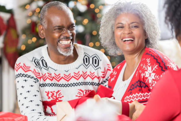 Happy senior couple spend Christmas with family Happy active African American senior couple wear Christmas sweaters on Christmas morning. They are opening presents with their adult daughter. christmas sweater photos stock pictures, royalty-free photos & images