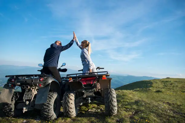 Beautiful couple is watching the sunset from the mountain sitting on quadbike.