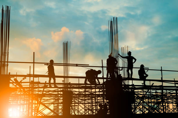 silhouette de l’équipe d’ingénieur et de la construction travaillent en toute sécurité sur un échafaudage sur immeuble de grande hauteur. au cours de pastel sunset arrière-plan flou pour le fond de l’industrie avec la foire light - land issues photos et images de collection