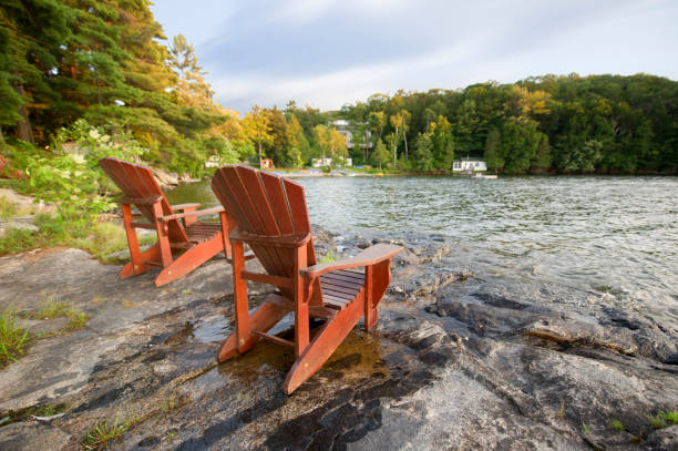 istock Two Muskoka chairs on a rock formation facing a calm lake 838477080