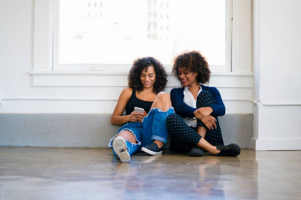 istock Two friends sitting on the floor looking at a mobile phone together 838486190