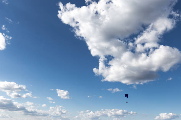 A paraglider flying against a deep, blue sky, with big white clouds