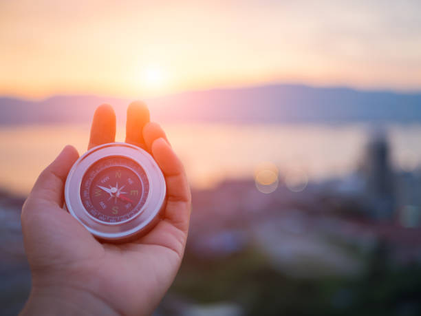 closeup hand holding compass with  mountain and sunset sky background. - compass symbol direction guide imagens e fotografias de stock