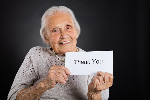 Portrait Of Smiling Elder Woman Showing Thank You Card Over Grey Background
