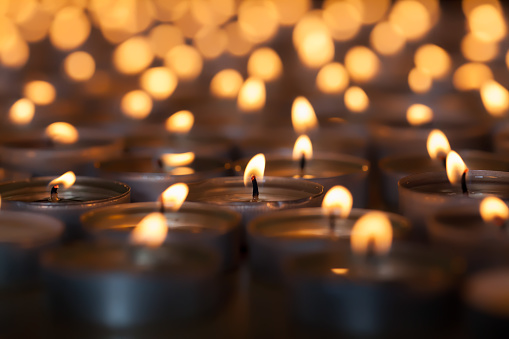 Lighted candle amongst hundreds of flaming tea light candles. Beautiful romantic candlelight. Selective focus on central lit wick.