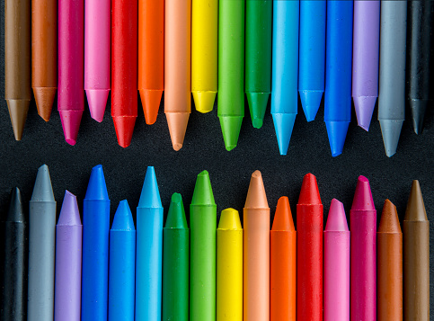 Wooden artists rainbow of drawing pencil crayons are laying in a straight line on a white marble background with copy space above them. The word pride is spelled diagonally across them in wooden letters to celebrate LGBT people.