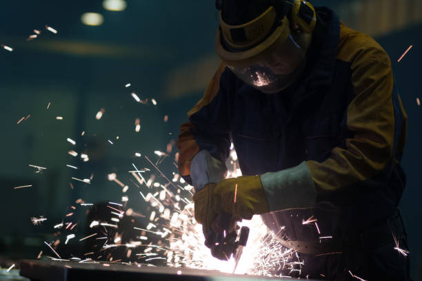 istock Heavy industry worker at a factory is working with metal on a angle grinder while hot sparks are produced in a result. 838527542