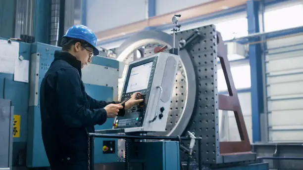 Factory worker is programming a CNC milling machine with a tablet computer.