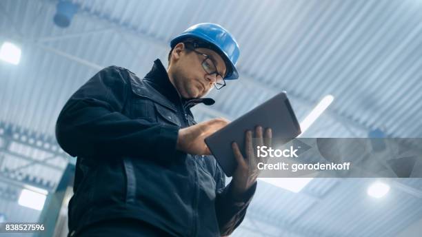 Trabajador De La Fábrica En Un Casco Está Utilizando Un Equipo Tablet Pc Foto de stock y más banco de imágenes de Gerente