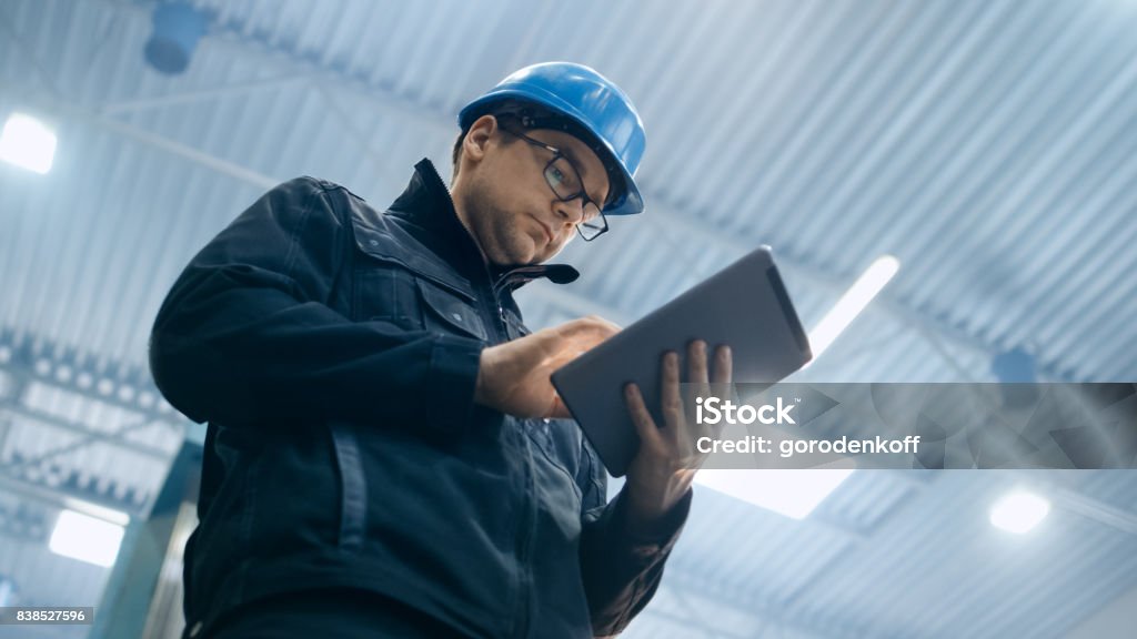 Factory worker in a hard hat is using a tablet computer. Manager Stock Photo