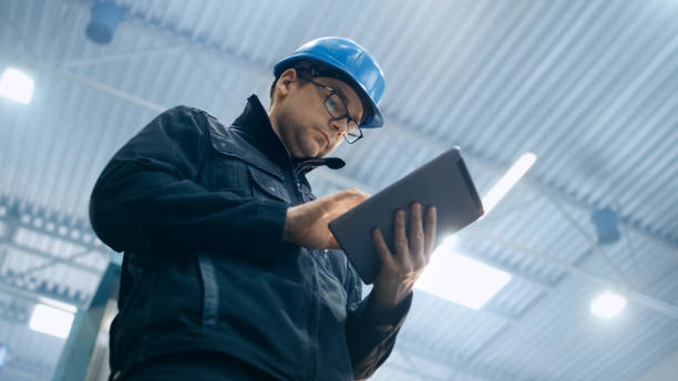 Factory worker in a hard hat is using a tablet computer. Factory worker in a hard hat is using a tablet computer. inspector stock pictures, royalty-free photos & images