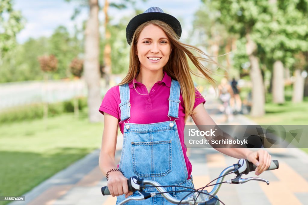 Beautiful young woman with her bicycle at the park Beautiful young happy woman smiling to the camera joyfully standing with her bicycle at the local park on a warm sunny day nature outdoors recreation activity happiness lifestyle hipster concept. Active Lifestyle Stock Photo