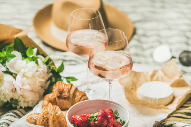 French style summer picnic setting and outdoor gathering concept French style romantic summer picnic setting. Flat-lay of glasses of rose wine with ice, fresh strawberries, croissants, brie cheese, straw hat, sunglasses, peony flowers. Outdoor gathering concept rose wine photos stock pictures, royalty-free photos & images