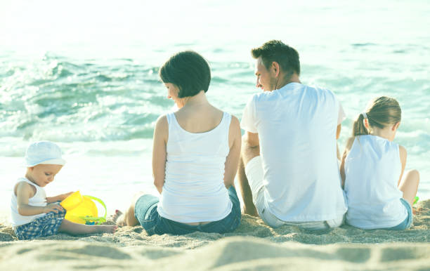 istock back view on family of four sitting on beach 838672902