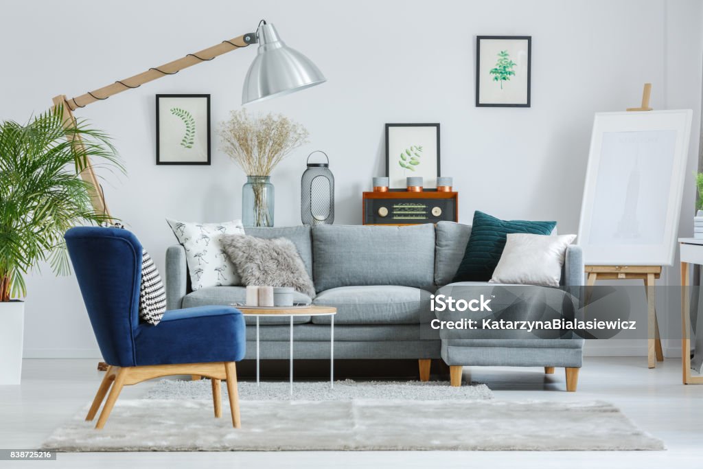 Blue armchair on grey carpet Blue armchair on grey carpet in designer's living room with lamp, easel and grey sofa Showroom Stock Photo