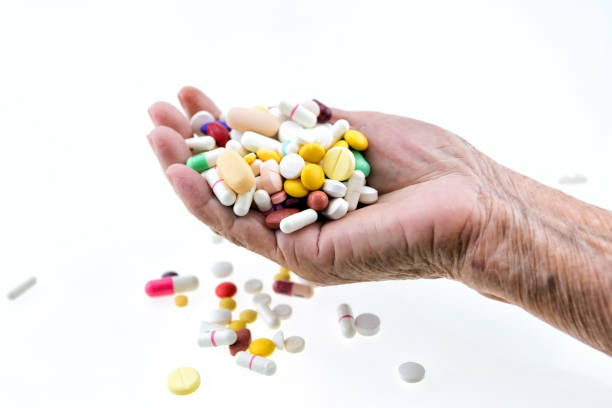 Many multi-colored pills in a Senior's hands on white background; Alzheimer's patients; caring for the health of the elderly patients stock photo