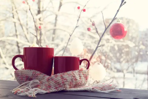 pair of red cups in a warming scarf against the window