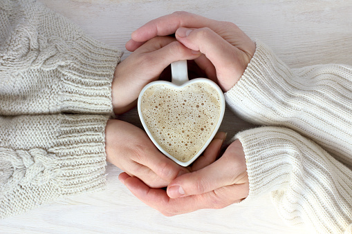 Coffee heart shaped in embraces pairs of hands