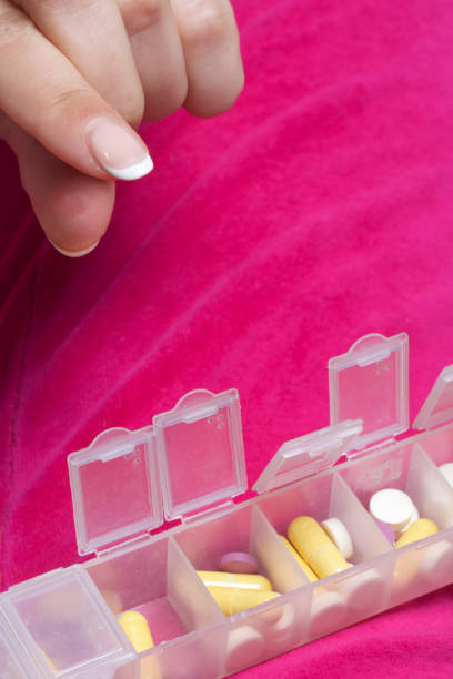istock Woman lying in bed taking pills from a special container. Holds a container and a pill. 838771770