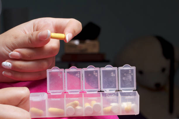 istock Woman lying in bed taking pills from a special container. Holds a container and a pill. 838771790