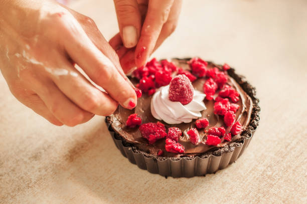 Woman chef preparing chocolate cake with whipped cream and raspberry. Close up