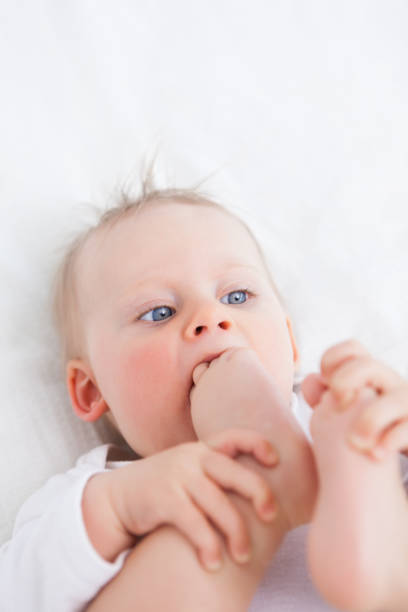 Cute baby placing her foot on her mouth while lying on a blanket