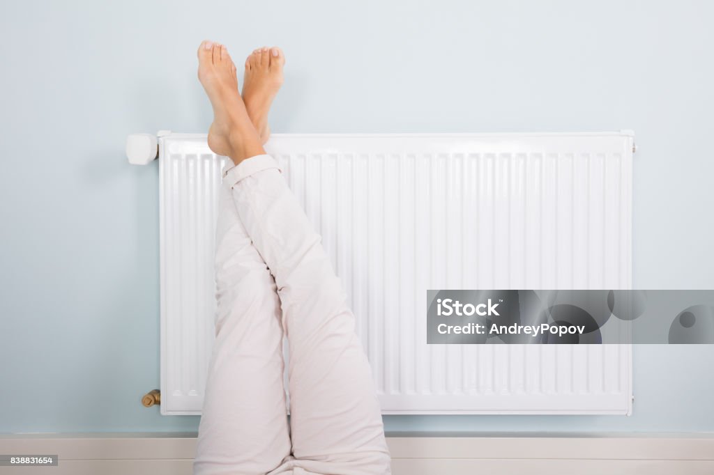 Mujer calentando sus pies en blanco radiador - Foto de stock de Radiador libre de derechos