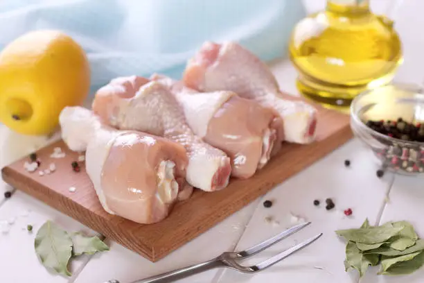 Raw chicken legs on the cutting board with spices, lemon and oil. Fresh poultry on the wooden table.