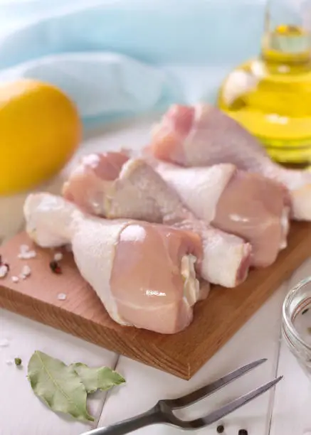 Raw chicken legs on a cutting board with fork and spices. Fresh hen meat for healthy diet.