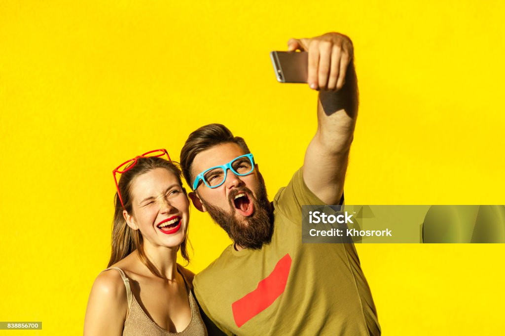 Couple de jeunes branchés macking selfie sur fond jaune - Photo de Selfie libre de droits