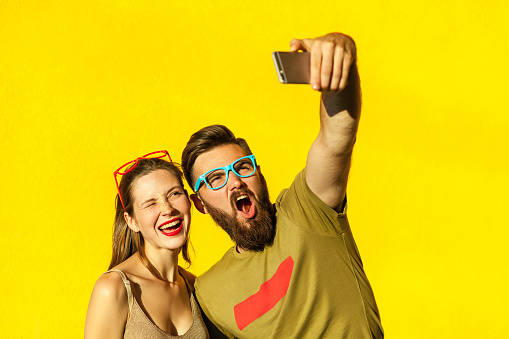 Hipsters couple macking selfie on yellow background. Studio shot